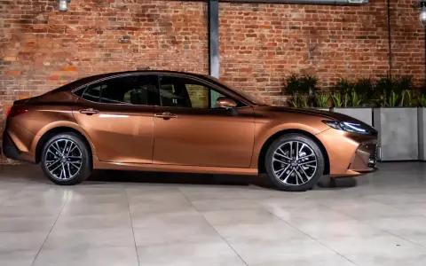 Elegancki, brązowy sedan auto z nowoczesnymi felgami stoi na tle ceglanej ściany.