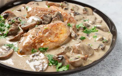 Un plat de poulet à la crème onctueuse, parsemé de champignons et de persil frais. Un délice crémeux qui invite à la dégustation.