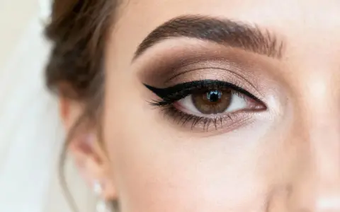 Oko kobiety z perfekcyjnym makijażem ślubnym glamour: brązowe cienie, wyraźna kreska i długie rzęsy.