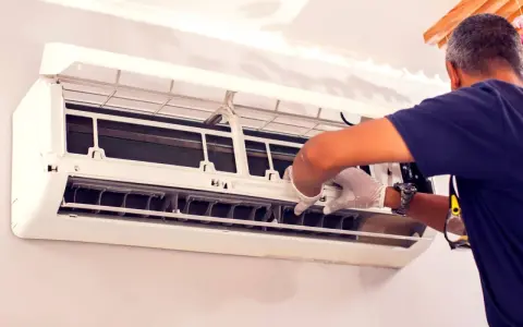 Un technicien en gants blancs effectue le nettoyage de climatisation, ouvrant l'unité pour accéder aux composants internes.