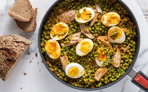 A skillet of peas and tuna with sliced hard-boiled eggs, served with bread.