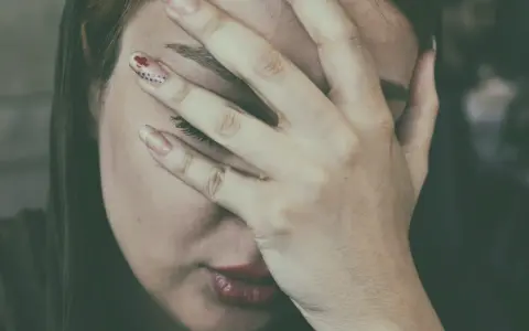 Kobieta zakrywająca twarz dłońmi, z widocznymi ustami i fragmentem oka.