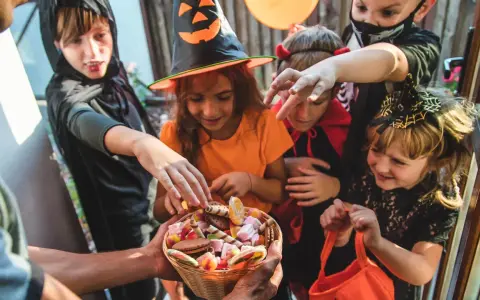 Barn i Halloween-kostymer sträcker sig efter godis ur en korg. Det är en klassisk "bus eller godis"-kväll!