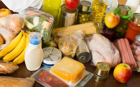 Variedad de alimentos, incluyendo frutas, verduras, pasta, latas y embutidos, que representan alimentos procesados y frescos.