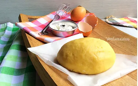 Impasto giallo pronto per essere lavorato, con uova e farina a lato. La pasta frolla senza burro è perfetta per dolci leggeri.