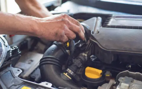 Ręce mechanika pracują przy silniku. Widoczny jest czarny przewód dolotowy i żółta zakrętka. p0101.