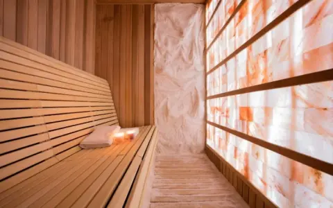 A serene salt sauna with a wooden bench, towels, candles, and a wall of glowing Himalayan salt bricks.