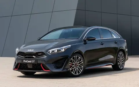 Stylowy, ciemnoszary Kia Proceed GT z czerwonymi akcentami i sportowymi felgami, zaparkowany przed nowoczesnym budynkiem.