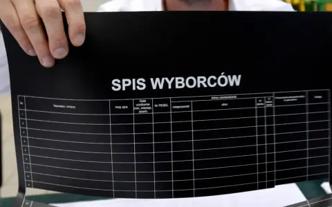 Ręce trzymają czarny dokument z napisem "SPIS WYBORCÓW". Widoczne kolumny do uzupełnienia, sugerujące dopisanie do spisu wyborców.