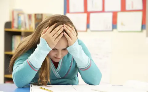 Verzweifeltes Mädchen mit Händen am Kopf im Klassenzimmer. Die **Kollektivstrafe Schule** lastet schwer auf ihr.