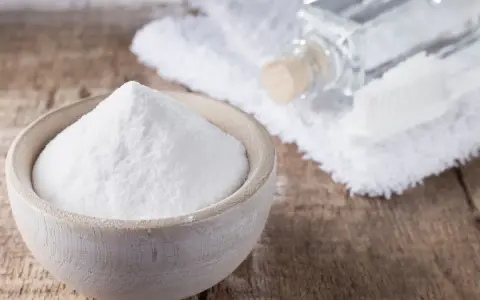Soda oczyszczona w miseczce, obok ręcznik, buteleczka i szczoteczka. Czy soda oczyszczona odbarwia ubrania?