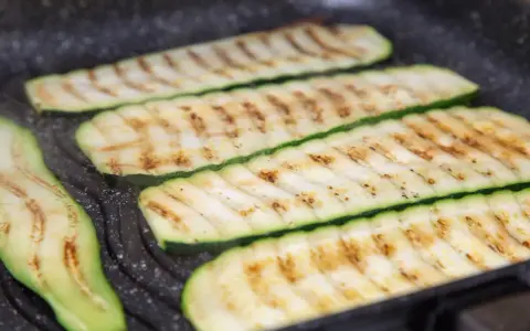 Fette di zucchine grigliate che cuociono su una piastra, con segni di grigliatura dorati e invitanti.