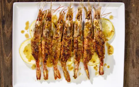 Gamberoni al forno dorati e croccanti, serviti su fette di limone e conditi con un sugo saporito.