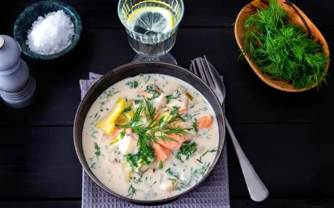 Krämig fisksoppa med lax och dill, en av många lyxiga fiskrecept. Serveras med citronvatten och havssalt.