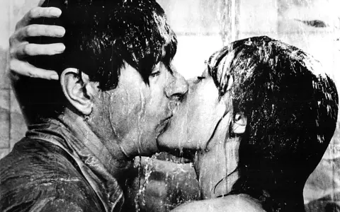 Una pareja se besa apasionadamente bajo la ducha, un momento íntimo que captura la esencia de qué es un beso francés.