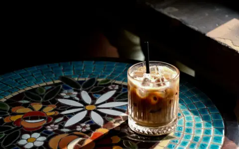 Orzeźwiający cold brew latte z lodem, podany na kolorowym, mozaikowym stoliku, w promieniach słońca.