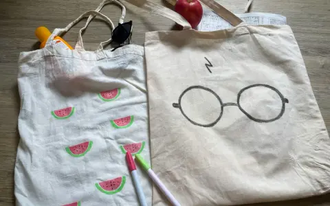 Zwei jute beutel bemalen: einer mit Wassermelonen, der andere mit Harry Potters Brille. Sonnencreme, Sonnenbrille und Stifte liegen daneben.