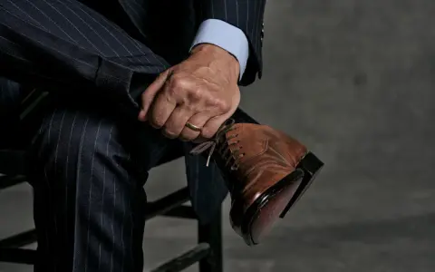 Un uomo con un abito gessato blu scuro e una camicia azzurra indossa eleganti scarpe stringate marroni.