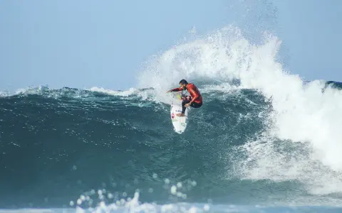 Surfer in rotem Neoprenanzug meistert eine riesige Welle beim Mauritius Surf.