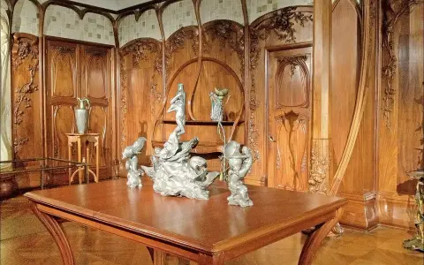 Intérieur Art Nouveau orné de boiseries sculptées, avec une table en bois et des sculptures, évoquant l'œuvre d'Alexandre Charpentier.