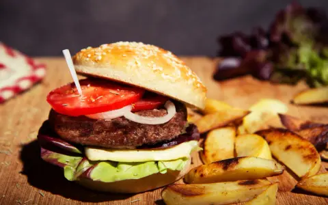 Burger maison avec pain aux graines, tomate, oignon, fromage et salade. Accompagné de frites. Une recette pain burger sans gluten à essayer !