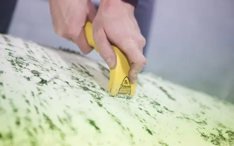 Mains utilisant un grattoir électrique antifouling pour enlever des résidus verts sur une surface.