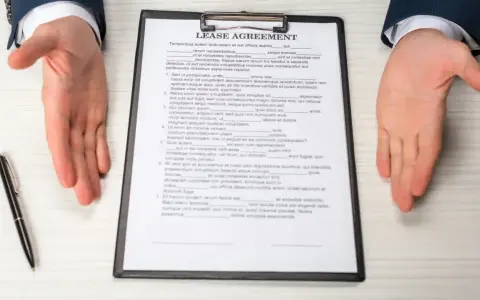 Dłonie wyciągnięte nad dokumentem "Lease Agreement" i długopisem.
