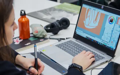 Studentka na studiach grafika Warszawa tworzy projekt na laptopie, używając tabletu graficznego.