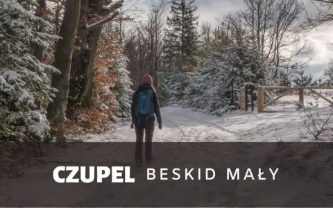 Kobieta w zimowej czapce i plecaku idzie zasypaną śniegiem trasą na Czupeł w Beskidzie Małym.