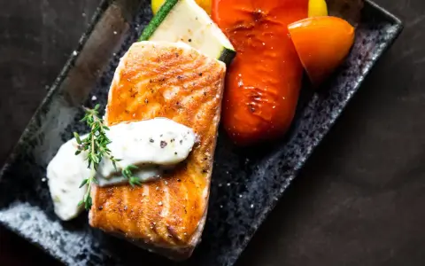 Pyszny łosoś wędzony na gorąco z sosem i pieczonymi warzywami na ciemnym talerzu.