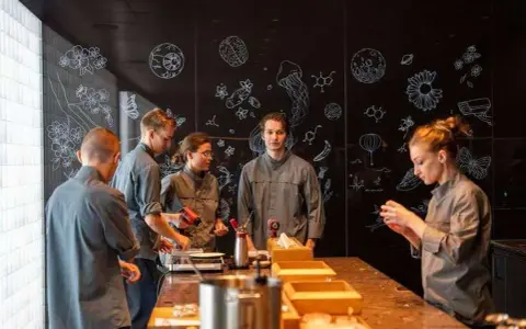 Une série de photos montrant une équipe en cuisine, devant un mur noir décoré de dessins scientifiques et floraux.