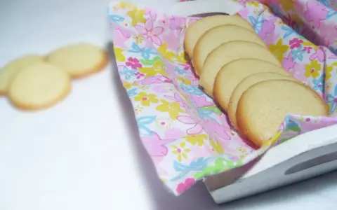 Delikatne biszkopty dla niemowlaka, ułożone na kolorowej tkaninie w kwiaty, na białej tacce.