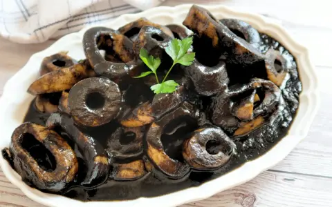 Calamares en su tinta, un plato tradicional español, servido en una fuente blanca con perejil fresco.