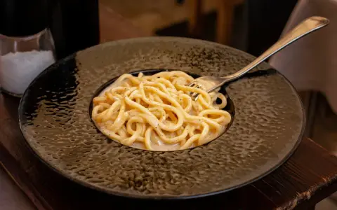 Pyszne cacio e pepe na czarnym talerzu, z widocznym młynkiem do pieprzu i solniczką w tle.