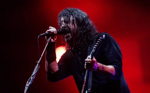 Dave Grohl z Foo Fighters na koncercie, śpiewający do mikrofonu i grający na gitarze.