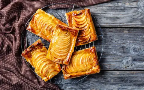 Deliziosi dolci con pasta sfoglia e mele caramellate, disposti su una gratella, su un tavolo di legno rustico.