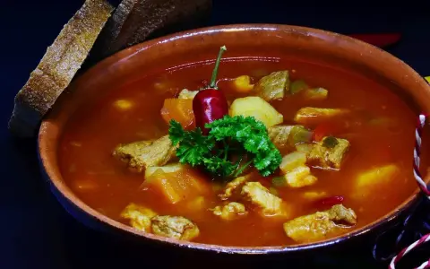 Pyszna zupa gulaszowa Ewy Wachowicz z kawałkami mięsa, ziemniaków i papryki, udekorowana papryczką chili i natką pietruszki. Podana z chlebem.