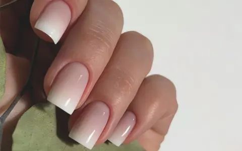 Mano con unghie curate e un effetto sfumato bianco e rosa, un esempio di nail art semplici ed eleganti.