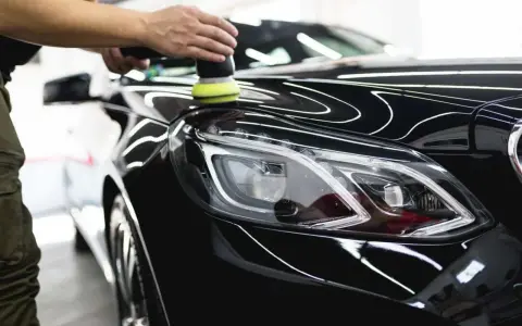 A person uses a polisher to wax a shiny black car, bringing out its deep gloss.