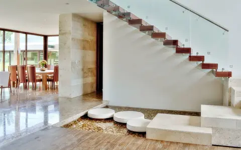 Escalera de madera flotante con barandilla de cristal. Ideas para decorar una escalera de madera con un estanque de guijarros y piedras.
