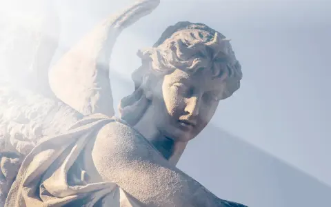 Kamienna rzeźba anioła, z promieniem światła padającym na twarz. Wzrok skierowany w dół, jakby w modlitwie do anioła stróża o pomoc.