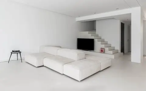 Soggiorno minimalista con divano modulare bianco e pavimento in resina lucida. Scale moderne integrano la TV.