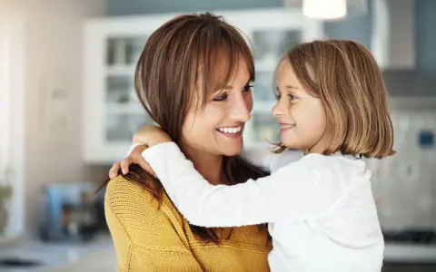Uśmiechnięta mama i córka przytulają się, emanując ciepłem i bliskością. To kwintesencja rodzicielstwa bliskości.