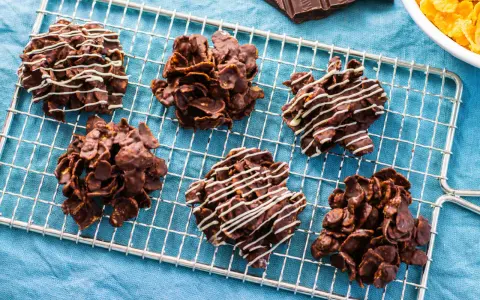 Sei dolcetti croccanti al cioccolato, simili a rose del deserto, raffreddano su una griglia. Alcuni sono decorati con sottili fili di cioccolato bianco.