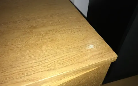 En ljus träyta, kanske ett fanerbord, med en liten vit fläck som behöver slipas.