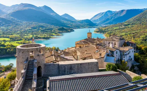 Borgo medievale con torre e lago turchese, incastonato tra i monti dell'Abruzzo.