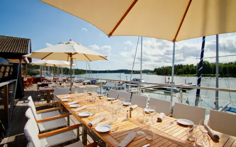 Väl dukade bord på en restaurang vid havet med segelbåtar i bakgrunden.