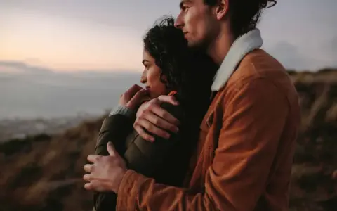 A couple embraces, looking out at a hazy landscape. This image shows how to feel more connected through shared moments and physical closeness.