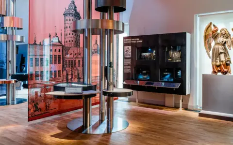 Utställning på ekonomiska museet med en stor illustration av en stad, en skulptur av en ängel och interaktiva displayer.