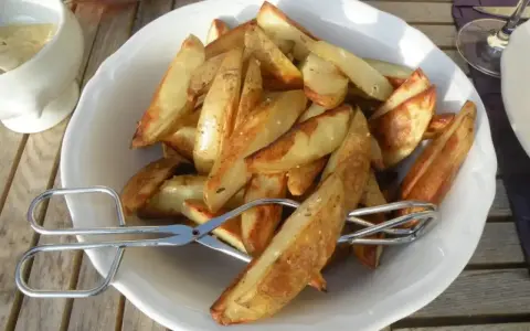 En skål med gyllene klyftpotatis i ugn, redo att serveras med tång.